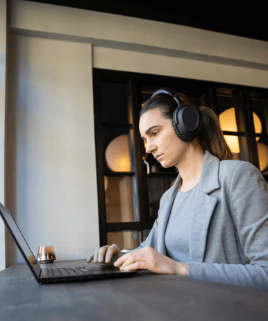Professional woman using headphones for farsi transcription services while working on laptop in modern office setting Professional woman using headphones for farsi transcription services while working on laptop in modern office setting