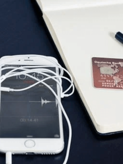  An Iphone with earphones wrapped around it, a visa shopping card placed beside it on a notebook