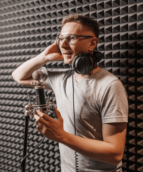 A multilingual Voice-Over Services artist records in a soundproof booth while a technician monitors clean audio levels.