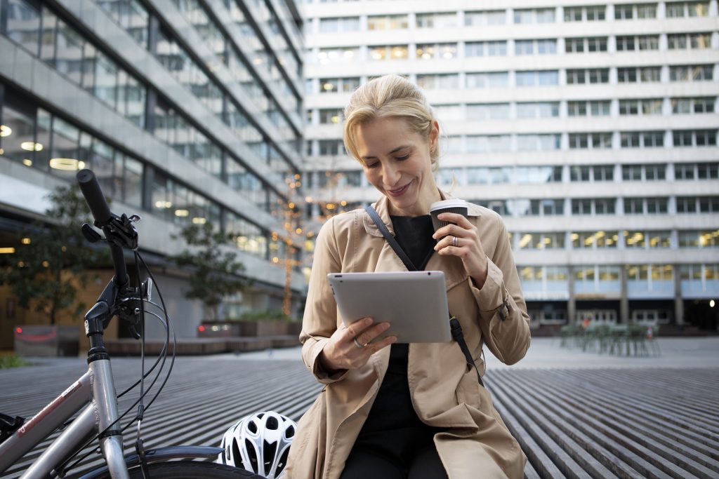 Woman working on her tablet outside and drinking coffee