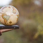 Closeup shot of a person holding bible with desk globe on top
