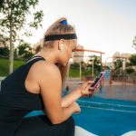 A Woman stands at the outdoor gym with a phone