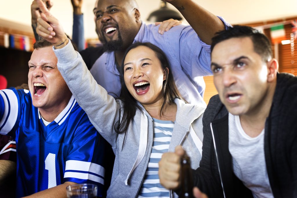 Diverse global sports fans from different countries celebrating an exciting moment while watching multilingual broadcast coverage