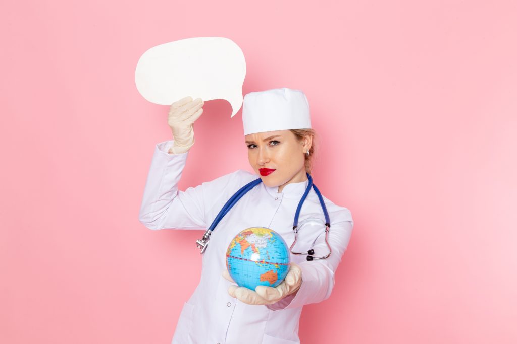 Front view young female doctor in white medical suit with blue stethoscope holding globe and white sign on the pink space medicine medical hospital health