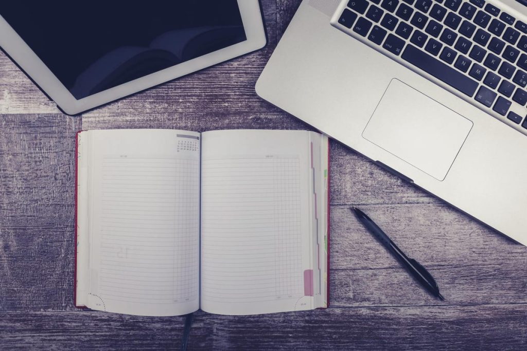 Stacks of handwritten notebook pages beside a laptop showing a neatly formatted manuscript in Word - Real Story: 155 Handwritten featured image