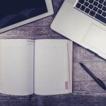 Stacks of handwritten notebook pages beside a laptop showing a neatly formatted manuscript in Word - Real Story: 155 Handwritten featured image