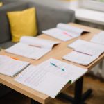 A stack of four multi-page documents on an office counter beside two printed certificates, one in English and one in Spanish - Real Story: Four People, featured image